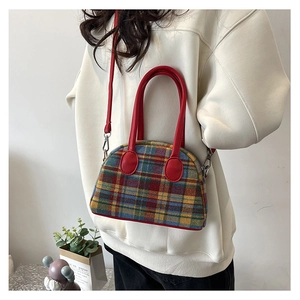 Detail of plaid fabric handbag with red leather straps held by model in casual setting