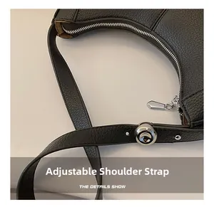 Detail of silver metal zipper and adjustable leather shoulder strap on black crossbody bag