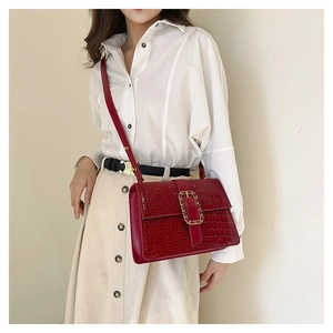 Detail of burgundy crocodile pattern crossbody bag with a gold buckle on a model