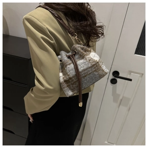 Detail of plush bucket bag with check pattern, leather drawstring, and golden hardware