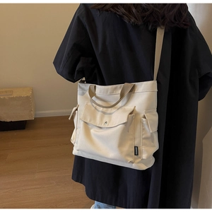 Detail of a beige canvas tote bag with side pocket and fashion woven label shown on model