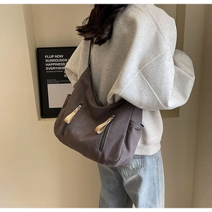 Detail of a dark brown canvas hobo bag showing texture and front zipper pockets on a model