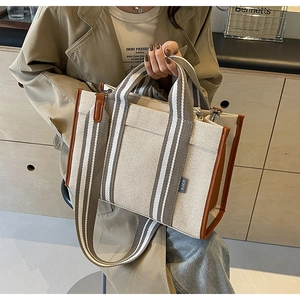 Detail of beige canvas tote with brown leather trim and striped shoulder strap texture