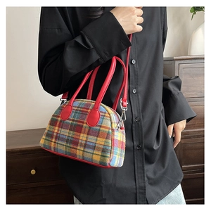 Detail shot of a plaid canvas handbag with red leather handles and metal zipper hardware