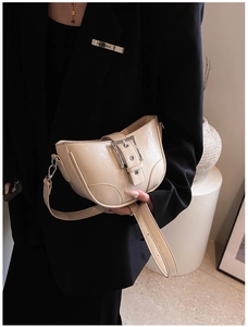 Détail d'un sac demi-lune crème avec une grande boucle argentée et une finition glacée