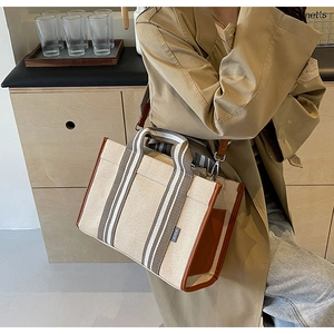 Detail of canvas crossbody tote with striped strap and brown leather trim on woman