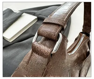 Detail of silver metal buckles and distressed brown leather texture on shoulder bag