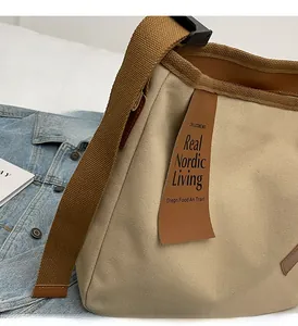 Detail of minimalist beige canvas crossbody bag with brown leather trim and wide fabric strap