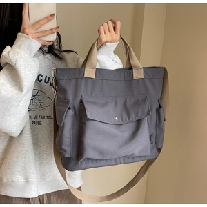 Detail of grey canvas tote bag with khaki straps and large front pocket with metal snap