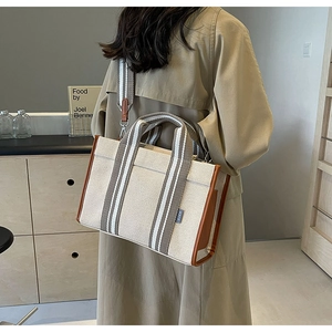 Detail of canvas tote bag with brown leather trim and striped shoulder strap