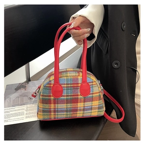 Close-up of tartan plaid handbag with red handles held by a model in a fashion setting