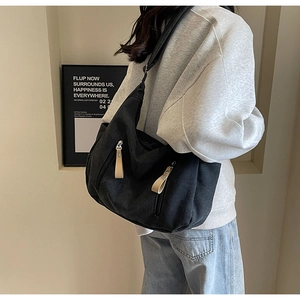 Detail of a large black canvas crossbody bag shown on a model in a minimalist setting