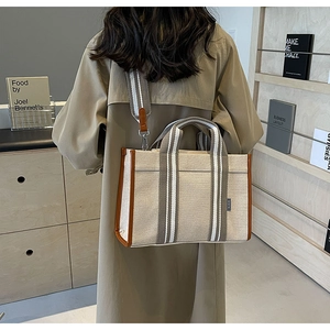 Detail of canvas tote bag with brown leather piping and striped strap worn by a model
