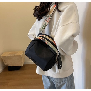 Dettaglio di una borsa a tracolla nera con cinturino in tessuto floreale su modella