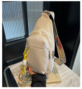 Close-up of cream nylon crossbody bag with colorful graffiti strap and yellow clip charm