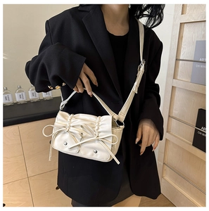 Detail of cream pleated PU crossbody bag with decorative bows on a black blazer