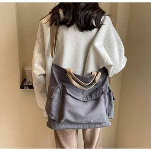 Detailed view of grey canvas crossbody bag showing side pocket and fashion woven label