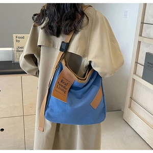 Close-up of blue canvas crossbody bag featuring adjustable brown woven strap and leather patch