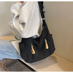 Detail view of large black canvas shoulder bag with dual zippered pockets and side pocket
