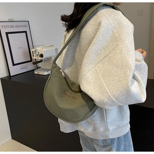 Détail du sac demi-lune vert armée en nylon avec broderie rouge porté par le mannequin