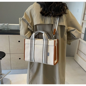 Detail view of canvas tote bag with brown leather trim and striped shoulder strap