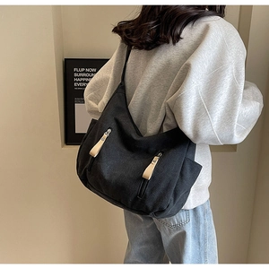 Close-up of black canvas shoulder bag with dual zipper pockets and beige pullers