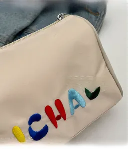 Gros plan détaillé du sac bandoulière en tissu beige avec broderie de lettres colorées