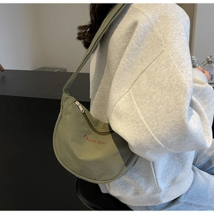 Détail du sac demi-lune vert sauge montrant le tissu en nylon et le logo brodé rouge