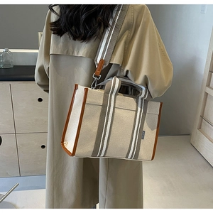 Detailed view of canvas tote bag with brown leather trim and striped shoulder strap