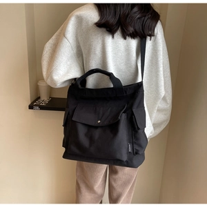 Detailed back view of a black canvas tote bag showing the side pocket and fashion tag