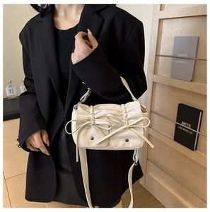 Detail of off-white pleated handbag with cute bows and adjustable shoulder strap
