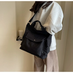 Detail of a large black canvas tote bag with front flap pocket and metal buckle for women