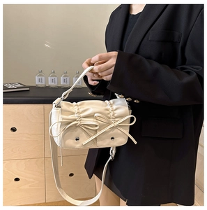 Detail of white pleated handbag featuring decorative bows and functional front pockets
