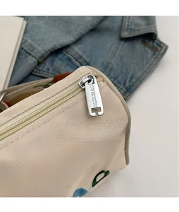 Détail macro du sac en sergé beige avec fermeture éclair argentée et broderies colorées