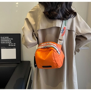 Dettaglio di una borsa a tracolla in nylon arancione con tracolla jacquard floreale su trench