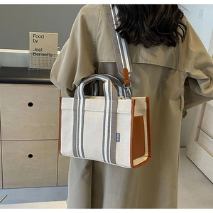 Detailed shot of beige canvas tote bag with brown leather trim and striped shoulder strap