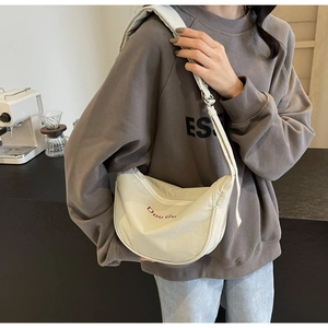 Sac bandoulière demi-lune crème avec broderie rouge porté par un mannequin dans un café