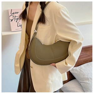 Detail of olive green crescent shoulder bag in lychee leather worn with a beige blazer