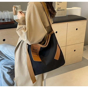 Detail shot of black canvas shoulder bag with brown leather labels in Nordic home setting