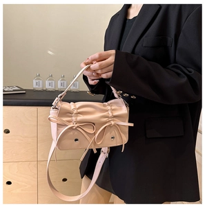 Close-up of light pink pleated handbag with ribbon detail worn over a black blazer
