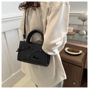 Close-up of a black leather handbag with bows worn by a model in a cafe setting