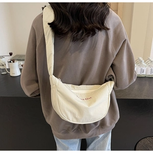 Détail du sac croissant crème montrant la texture du tissu léger et le logo imprimé rouge
