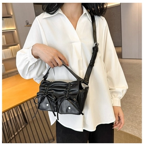 Detail of black pleated PU handbag featuring dual bow pockets and a long strap