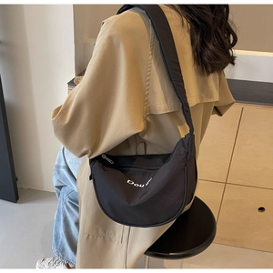 Détail du sac croissant en nylon noir à large bandoulière sur un trench-coat beige