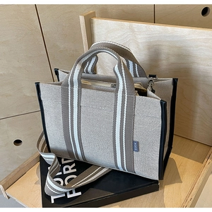 Minimalist beige and brown canvas tote bag with striped straps on a stylish book