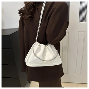 Close-up of white PU cloud bag with silver chain strap worn over a brown blazer