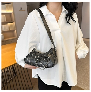 Detail of a vintage black PU shoulder bag with silver eyelets and chain on a model