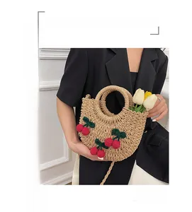 Close-up of handmade woven straw handbag with red knitted cherry charms and round handle