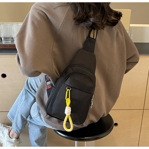 Detail view of black nylon crossbody bag with dual zippers and yellow braided charm