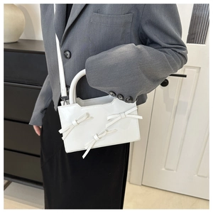 Detail view of a white glossy PU handbag with decorative bows and adjustable shoulder strap